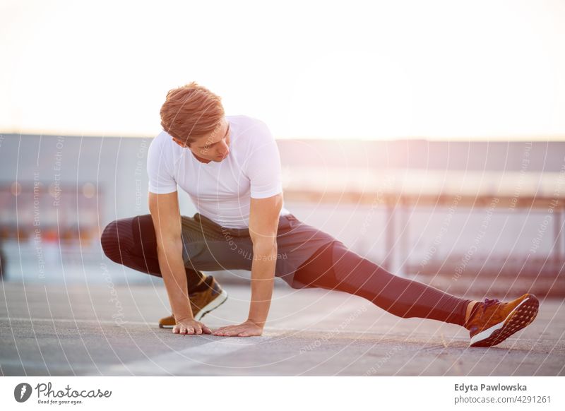 Young man doing stretching exercise in urban area Jogger runner jogging running people young male energy clothing exercising fitness recreation sport
