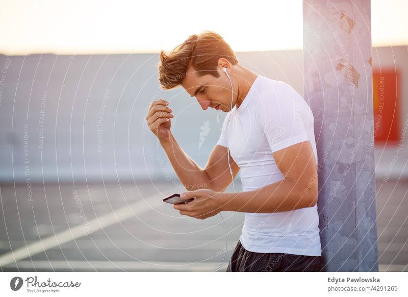 Young man checking his smartphone before exercising mp3 player music listening earphones app radio monitor progress mobile phone technology Jogger runner