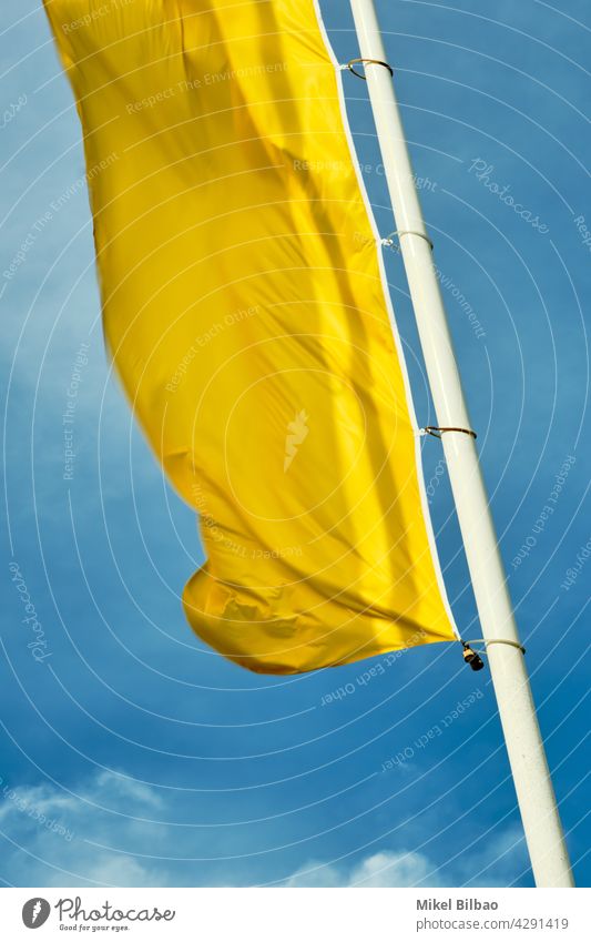 yellow flag on a pole over blue sky. waving wind windy ornament colourful colours background fabric cloth material pattern culture color colors colorful object