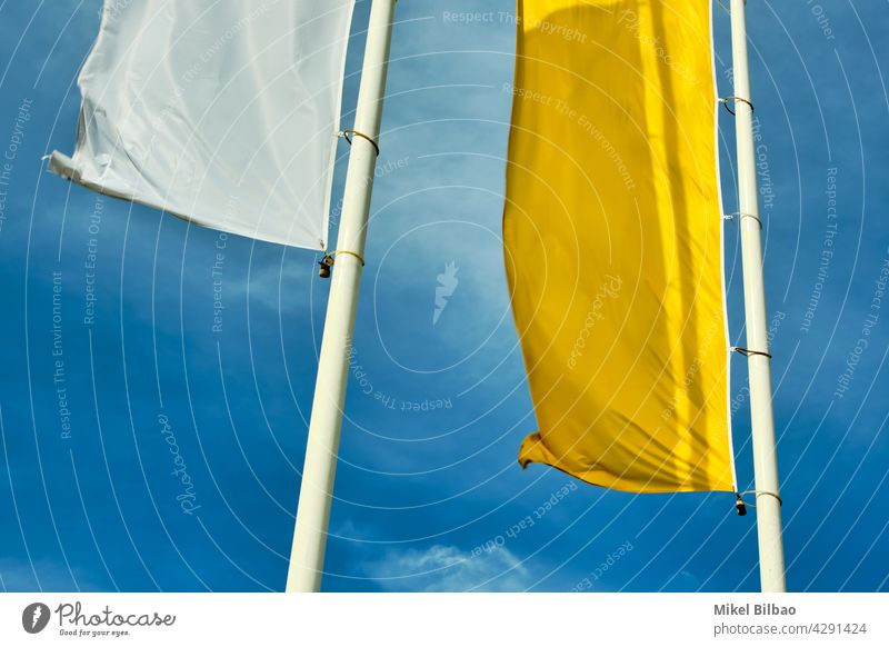 white and yellow flags on a pole over blue sky. wind windy waving ornament color colour colors colours colorful background fabric cloth material pattern culture