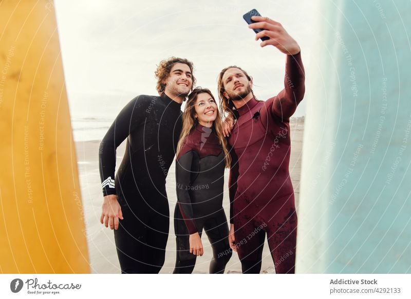 Surfer friends at the beach with surfboards taking selfie with mobile phone athletes smile sand seashore smartphone sport activity happy lifestyle water