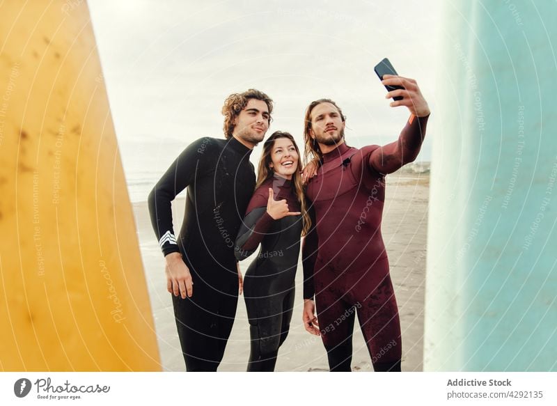 Surfer friends at the beach with surfboards taking selfie with mobile phone athletes smile sand seashore smartphone sport activity happy lifestyle water