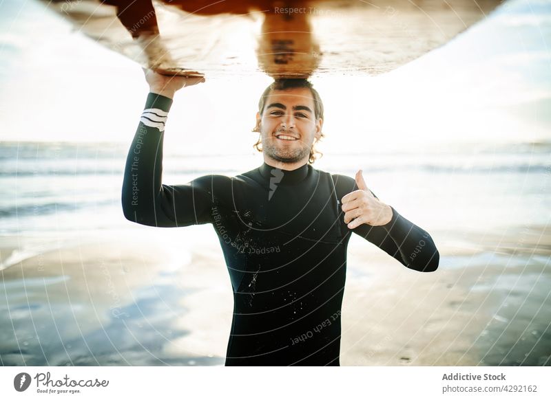 Smiling surfer at the beach carrying surfboard man nature sunset portrait smile wave outdoors wetsuit seacoast male thumbs up happy cool sportsman surfing hobby