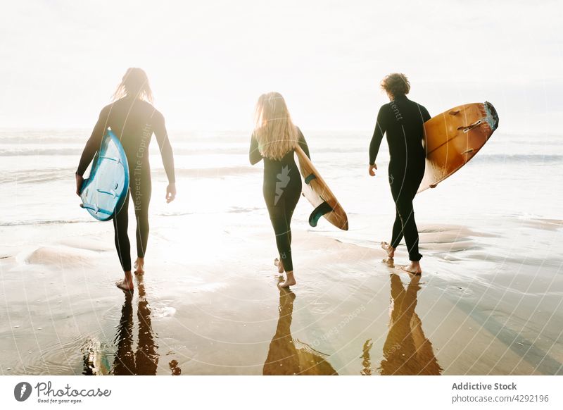 Anonymous surfer friends at the beach with surfboards nature sunset wave outdoors wetsuit seacoast together surfing hobby ocean woman men people seaside young