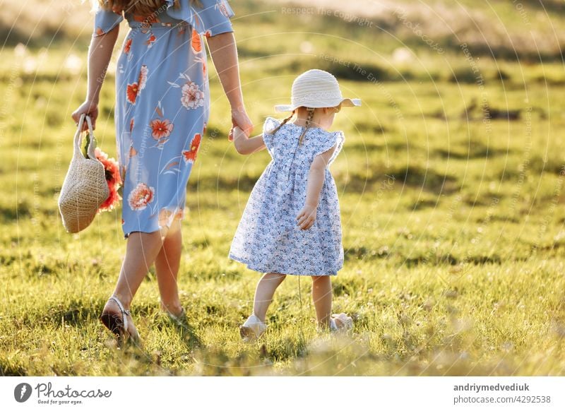 Young mother walking with her little daughter in the green field. Family holiday in garden. Portrait mom with child together on nature. Mum, little daughter outdoors. Happy Mothers Day. Close up