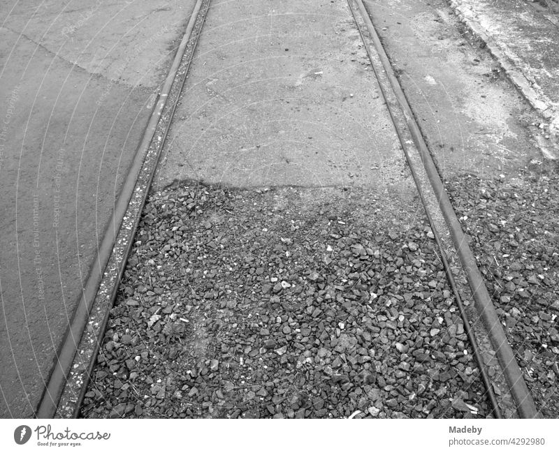 Old rails in ballast and asphalt or former port railway at the old inland port in Offenbach am Main in Hesse, photographed in classic black and white