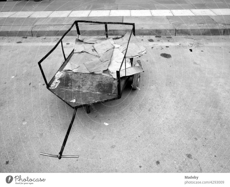 Old dilapidated handcart with cardboard scraps next to the curb on the side of the road in Göynük, Bolu province, Turkey, photographed in neo-realist black and white
