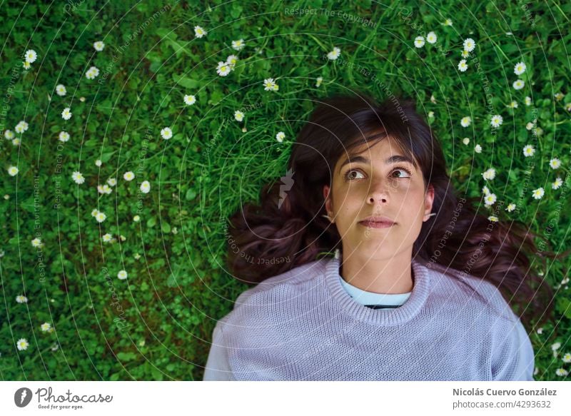 Hopeful young woman looking up lying on the grass surrounded by small flowers. person nature relaxation green portrait copy space smiling caucasian happiness