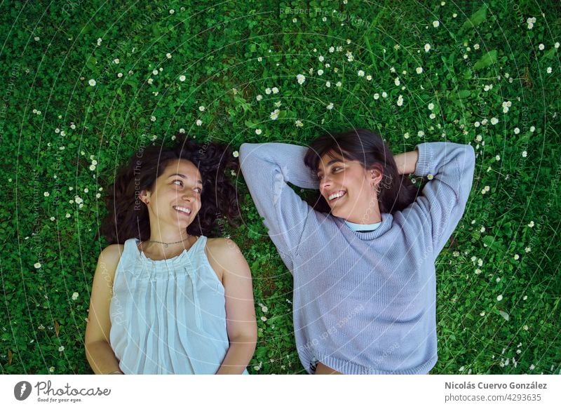 Two young women looking at each other lying on the ground. real people person couple happy together love lesbian lifestyle friends relax smile woman rest