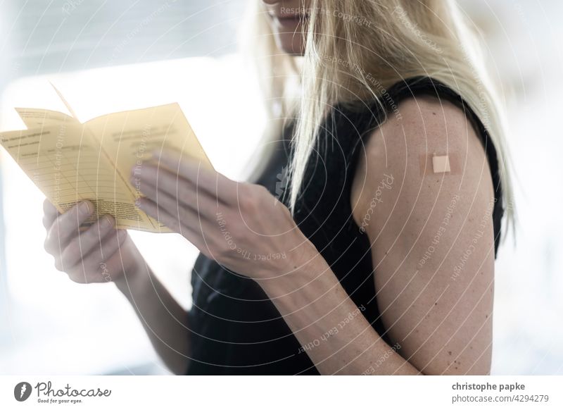 Blonde woman holding vaccination card and has plaster on upper arm after vaccination Woman Immunization Vaccination card corona coronavirus covid-19 pandemic