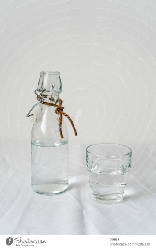 Glass bottle and a drinking glass with water on a white tablecloth Water White Drinking Beverage Cold drink Bottle Fresh Drinking water Healthy Summer Thirst