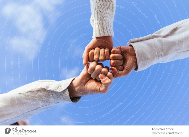 Crop people stacking hands under blue sky friend close bump fist support together group freedom sunlight summer bright team power trust relationship help