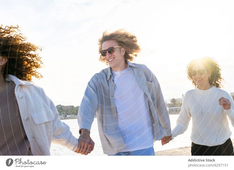 Laughing curly friends holding hands on seashore group together cheerful stroll carefree style happy vacation relationship summer beach harmony freedom nature