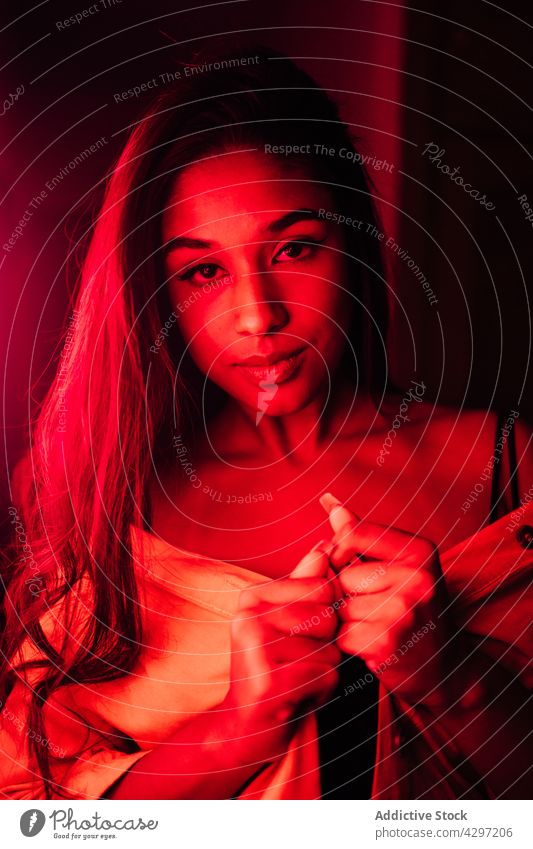 Young attractive Hispanic woman on terrace at night rest neon red light style dark female young illuminate relax joy ethnic positive lingerie vivid vibrant
