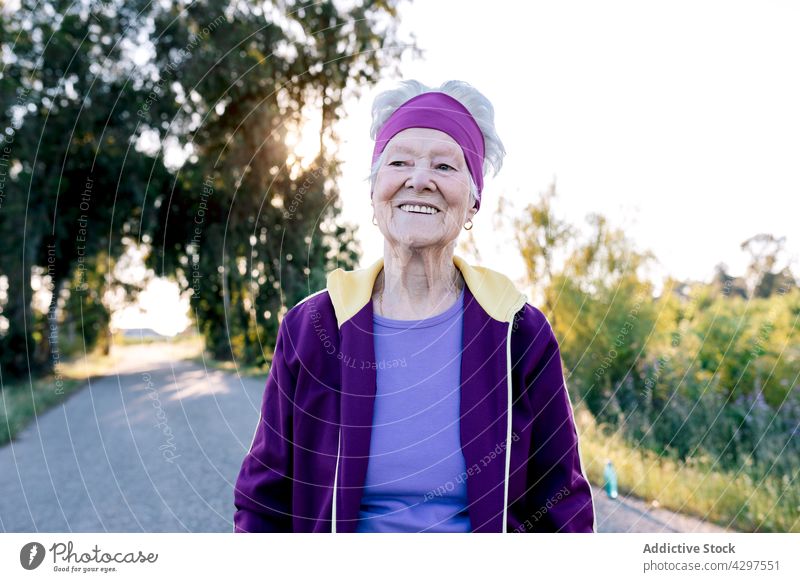 Positive elderly sportswoman smiling and walking training countryside fitness morning healthy summer road smile female jogger aged senior happy workout activity