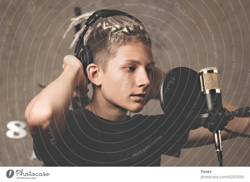 Stylish attractive guy with dreadlocks is recording a song in the studio. A young singer in black studio headphones stands in front of a microphone. Generation Z young talent