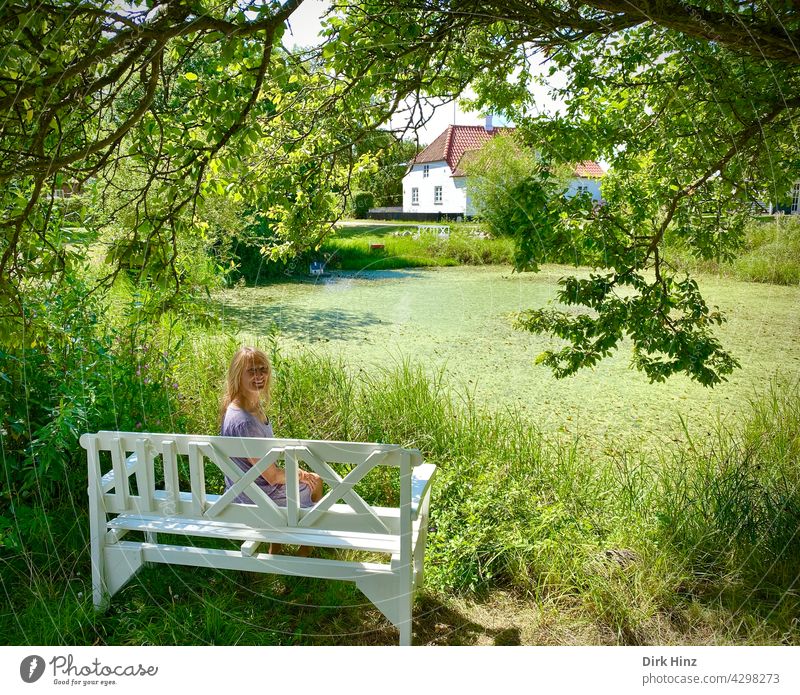 Attractive blonde woman sitting on white bench under oak tree by pond Woman pretty Feminine Adults Exterior shot Human being Idyll Denmark Pond Summer