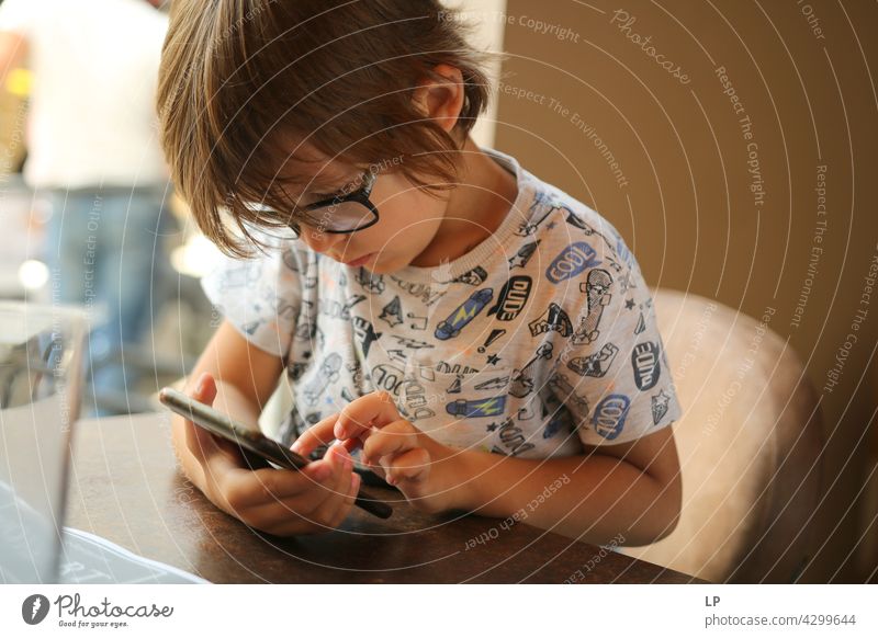 Boy wearing glasses and looking at a display of a mobile Parenting homeschooling surfing the net watching cartoons resting connection using phone enjoyment