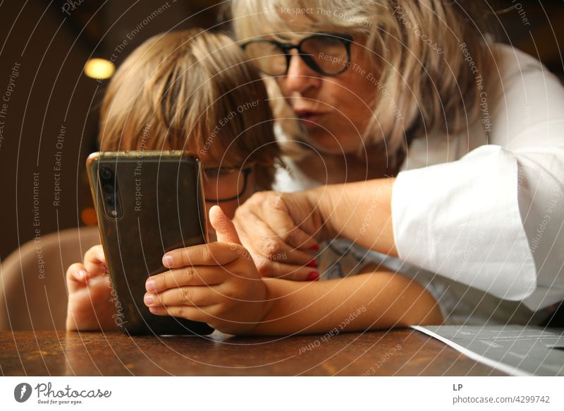 Boy wearing glasses and looking at a display of a mobile under the supervision of an adult Parenting homeschooling surfing the net connection using phone