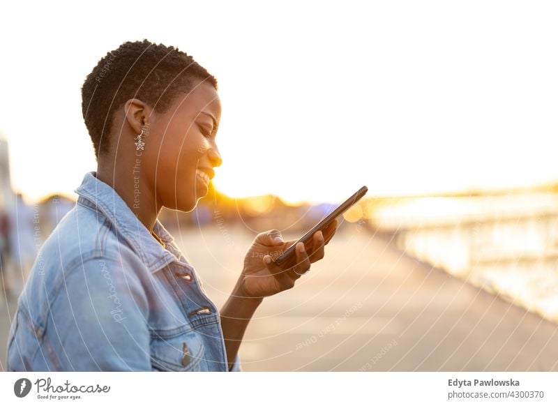 Smiling young woman using smartphone outdoors afro proud real people city life African american afro american student Black ethnicity sunny sunset outside