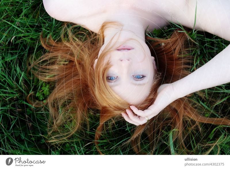Portrait of a beautiful young sexy redhead woman spreading red hair fan-shaped lying with bare shoulders relaxing on the green grass, copy space Redhead upside