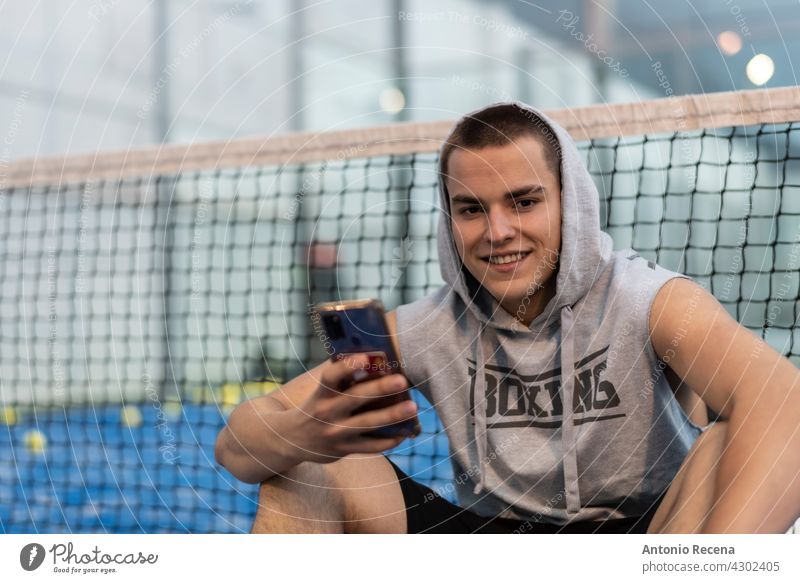 Young man with urban style takes a break with the phone trains after playing paddle tennis on an outdoor court young training padel sport ball racket net