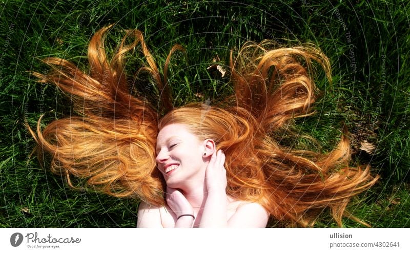 Beautiful portrait of a young sexy red-haired woman, lying in the summer sun in happiness, laughing, relaxing on the green grass, the red hair draped freely around the head. Copy space