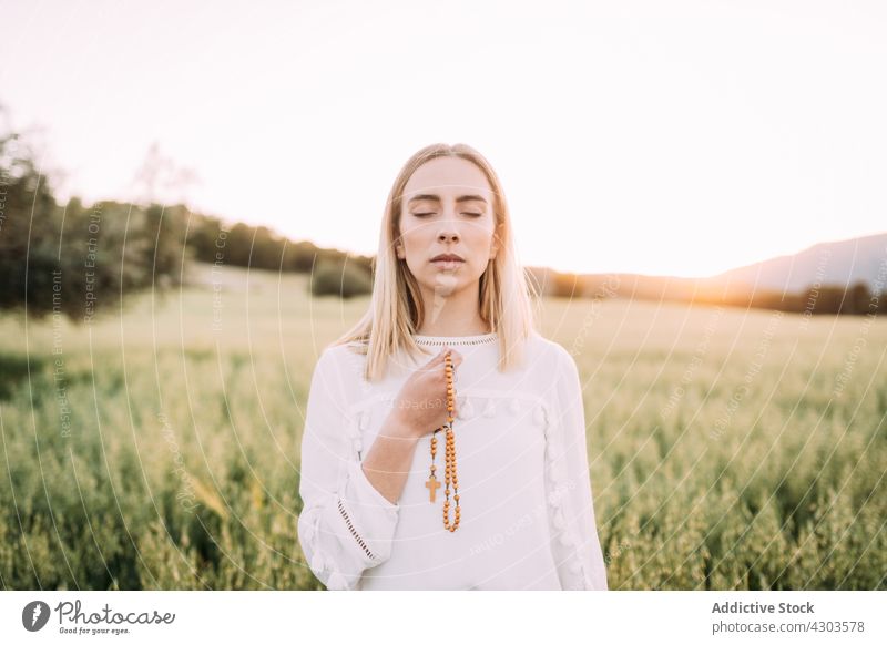 Calm female praying with cross in field woman nature calm faith belief harmony peace tranquil religion wish serene meadow rural pure white dress eyes closed
