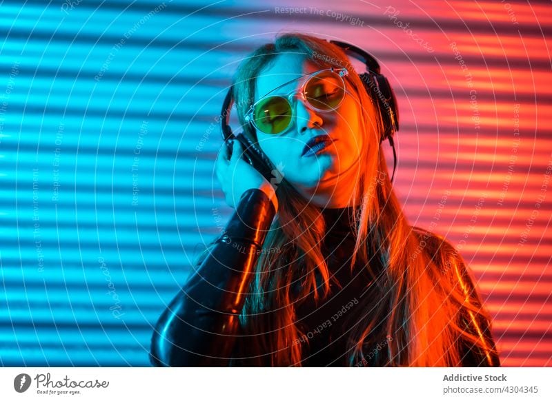 Woman listening to music under neon illumination woman smile blue red illuminate modern entertain bright female young gesture joy gadget headphones sound song