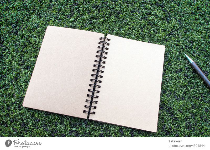 Kraft paper spiral notebook with pen on the Artificial turf blank kraft brown clean empty template page object document pad diary space pencil grass texture