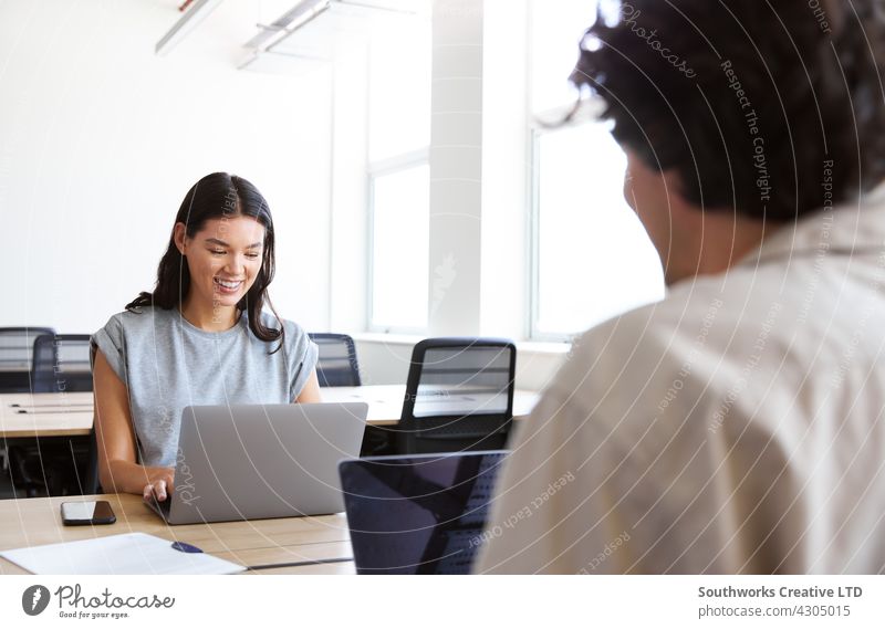 Young couple with laptops at desks working on start up business in rented open plan office space woman young meeting informal casual talking modern co-working
