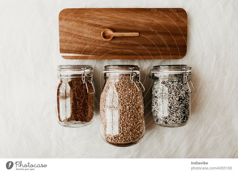 Glass jars full with dried uncooked food ingredients and wooden spoon on brown tray glass isolated container white seed bottle sesame seed cereal spice healthy
