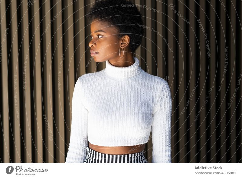Young African American female near striped building wall woman smile happy style urban street city outfit fashion african american black ethnic young earring