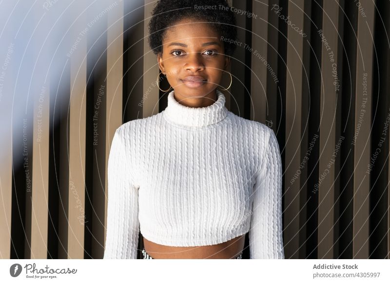 Young African American female near striped building wall woman style outfit modern urban city street casual portrait appearance fashion model crop sweater
