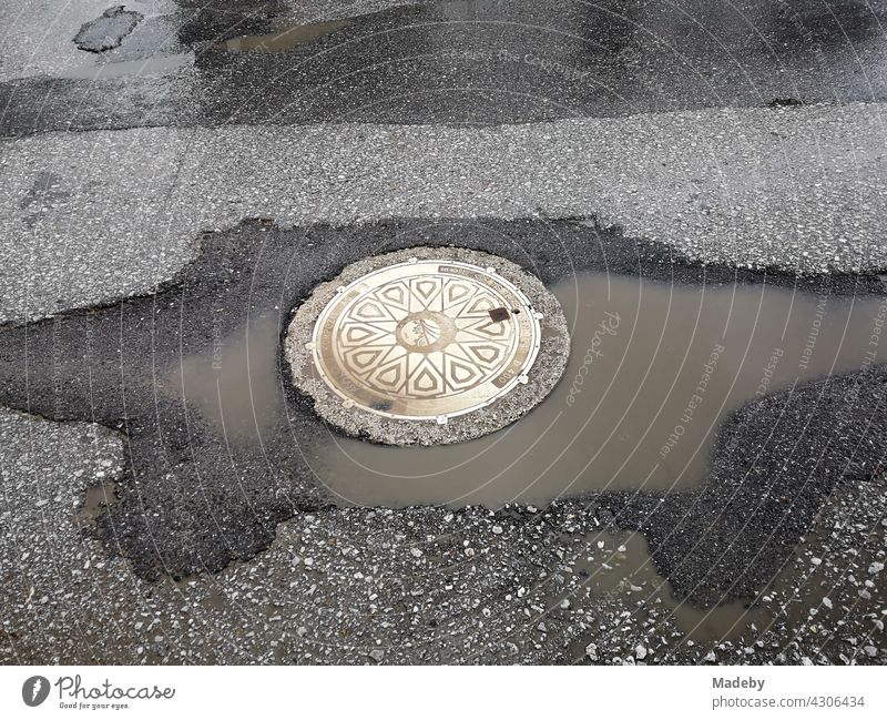 Beautifully decorated round manhole cover with large puddle in the sunshine after a rain shower in Adapazari, Sakarya province, Turkey Manhole cover Channel lid