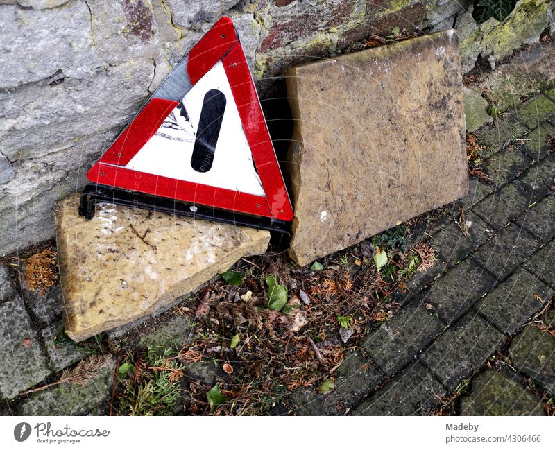 Broken old warning triangle at the roadside in front of an old wall in autumn in the old town of Oerlinghausen near Bielefeld in the Teutoburg Forest in East Westphalia-Lippe