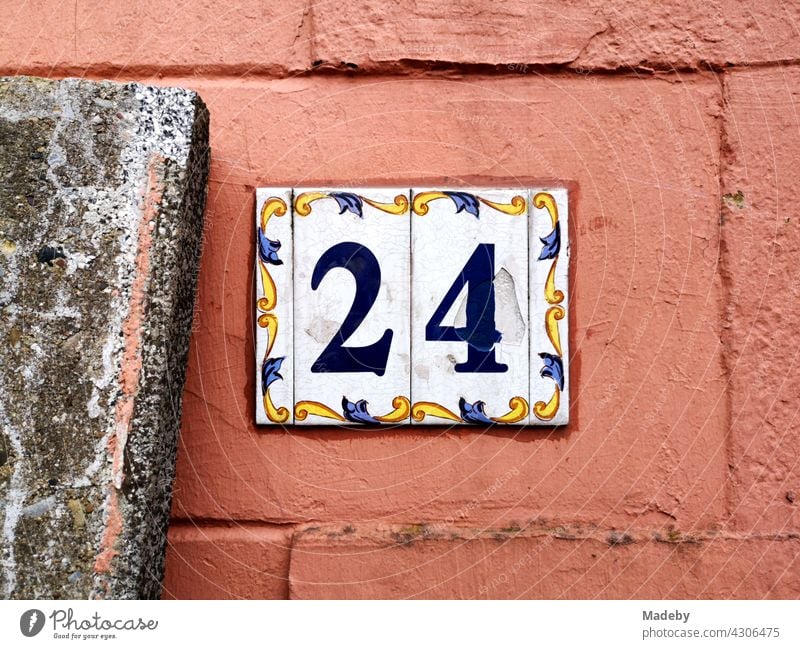 House number 24 as sign made of enamel with decoration and ornament on old facade in orange in Oerlinghausen near Bielefeld in the Teutoburg Forest in East Westphalia-Lippe