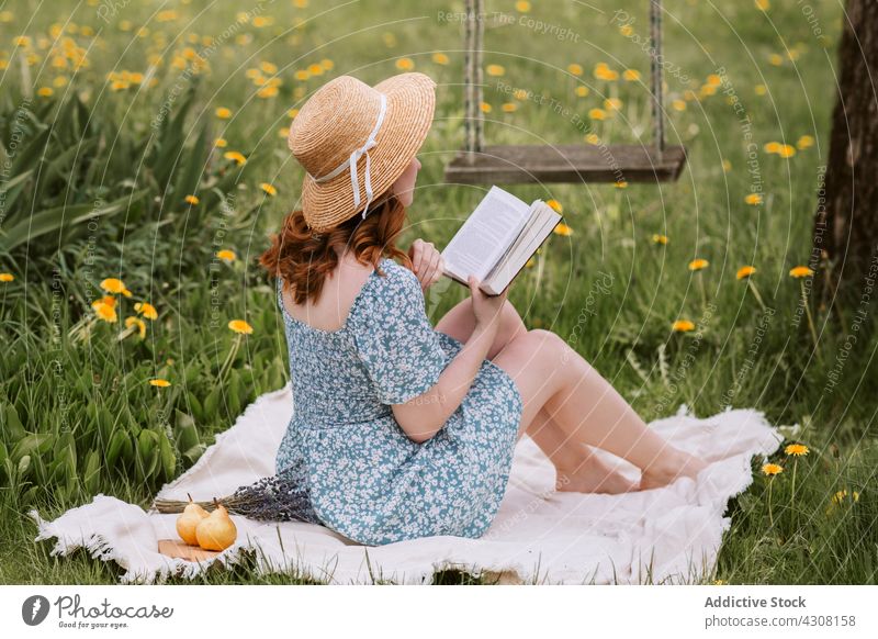 Woman with book resting on picnic blanket in nature woman read summer novel straw hat meadow relax female countryside grass weekend dress story leisure