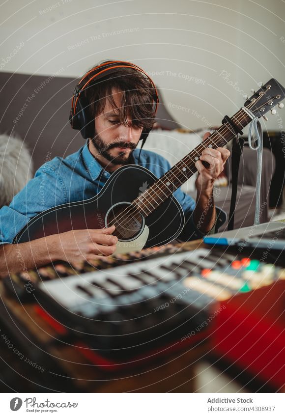 Musician playing on guitar near laptop at home musician headphones man young table synthesizer studio device gadget equipment instrument acoustic player