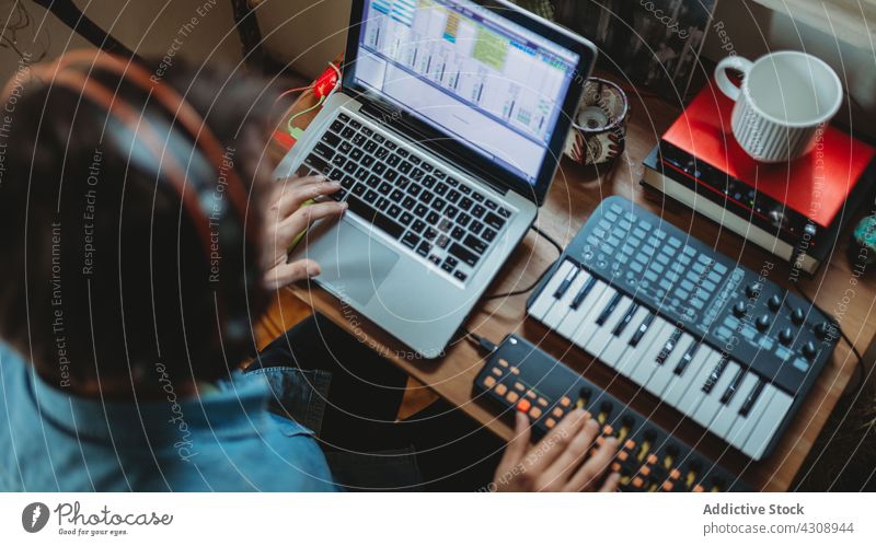 Anonymous musician using synthesizer and laptop at home headphones man young table studio device gadget equipment player recording room apartment leisure audio