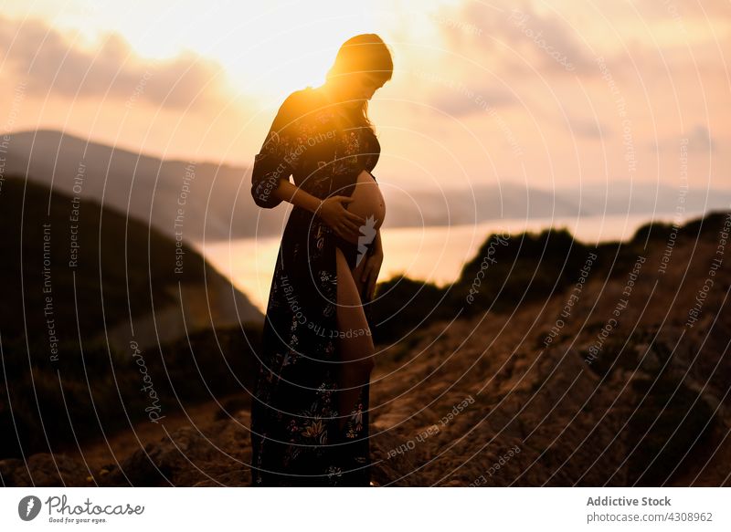Pregnant woman standing on hill at sunset pregnant silhouette mountain peaceful expect nature mother dream belly maternal female tummy calm anticipate harmony