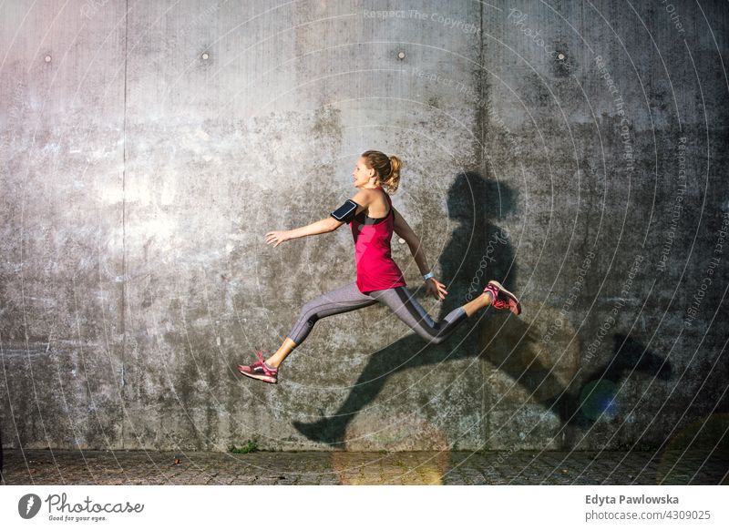 Young woman jumping against grey wall leaping action healthy dance exercise flexibility Jogger runner jogging running people young female energy clothing