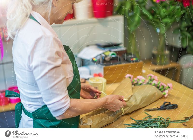 Woman working in florist shop Florist flower flowers bunch bouquet holding people adult senior mature woman female beautiful attractive smiling happy apron