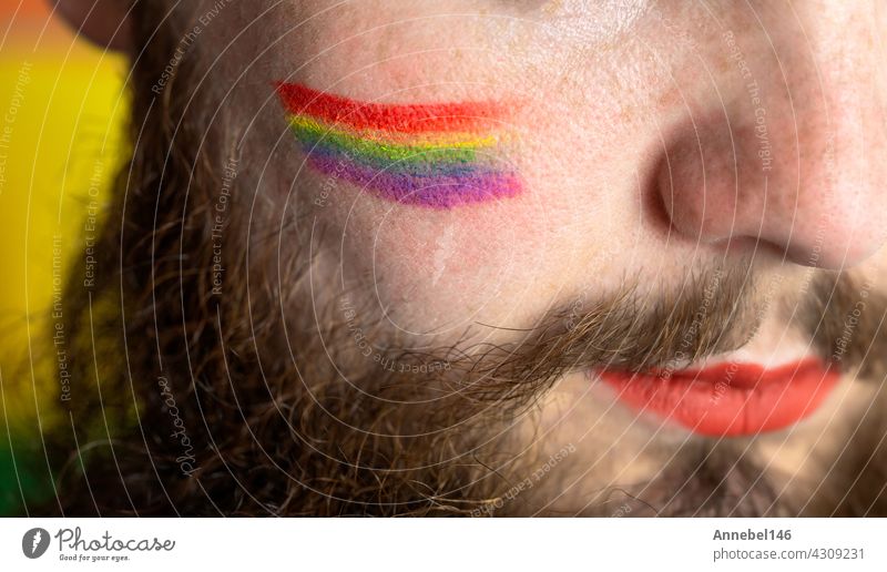 Young handsome bearded man with pride flag on his cheek, rainbow flag standing for LGBTQ, Gender right and sexual minority. Portrait lgbt homosexual equality