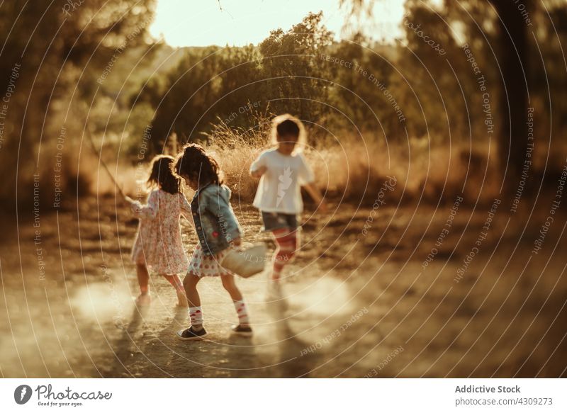 Little kids having fun in puddle children nature summer friend group play together carefree happy jump girl playful childhood freedom friendship active little
