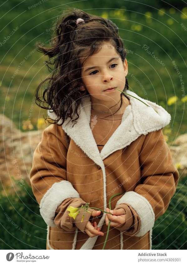 Cute ethnic girl in outerwear standing in nature kid spring coat pensive cute flower child little childhood thoughtful grass bloom adorable calm female season