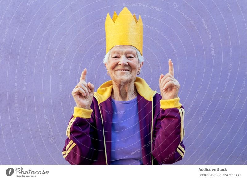 Smiling elderly sportswoman in decorative crown with fingers up finger up queen smile attentive friendly indicate concept portrait handmade paper material