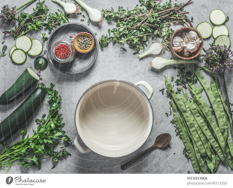 Various healthy green ingredients on concrete kitchen table with spices and white cooking pot, top view. Vegan food various vegan food dinnerware setting