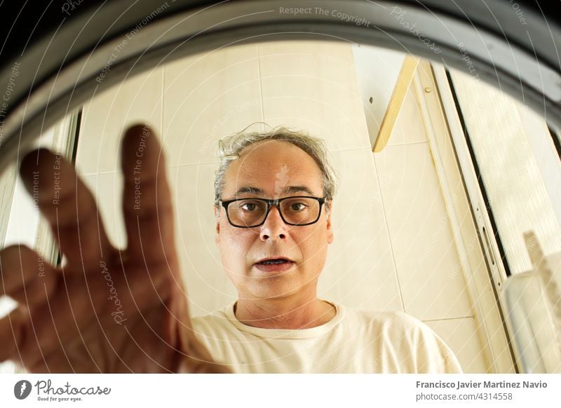 mature man doing laundry seen from inside the washing machine inside view clothes clothing home male horizontal chore door person caucasian drum indoor white