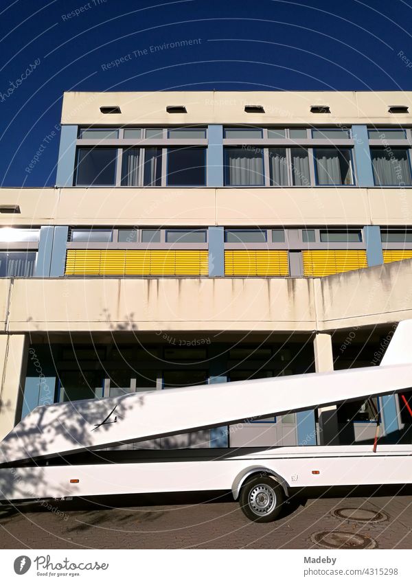 Weißer Anhäger für Segelflugzeuge vor einem modernen Schulgebäude mit gelben Jalousien im Sommer bei Sonnenschein in Oerlinghausen bei Bielefeld im Teutoburger Wald in Ostwestfalen-Lippe